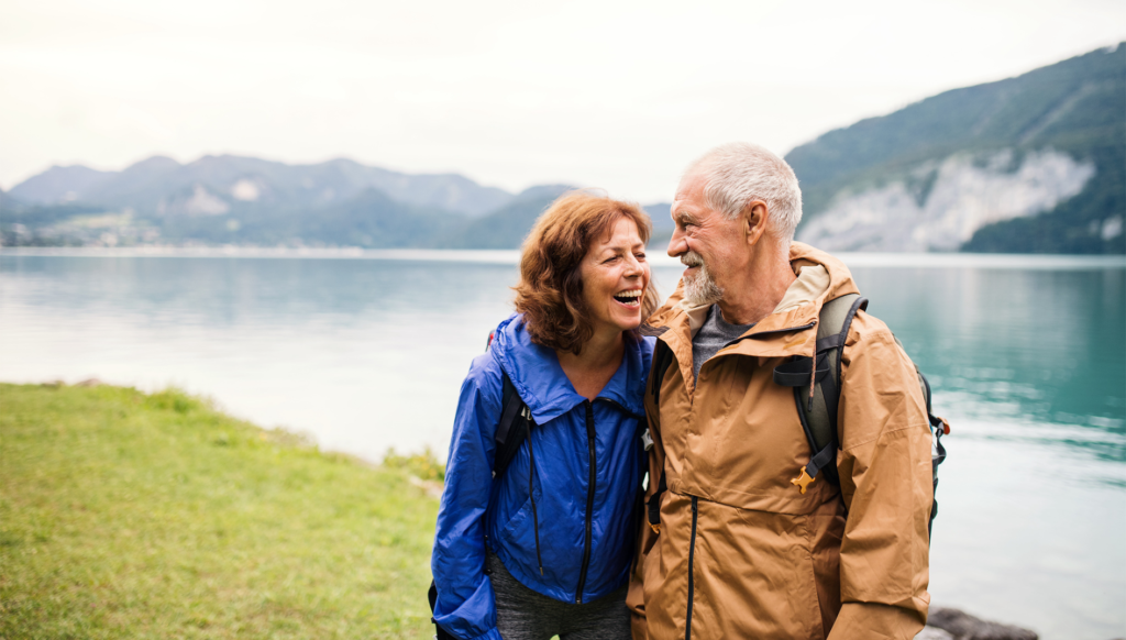 A senior pensioner couple walking by lake in nature, smiling